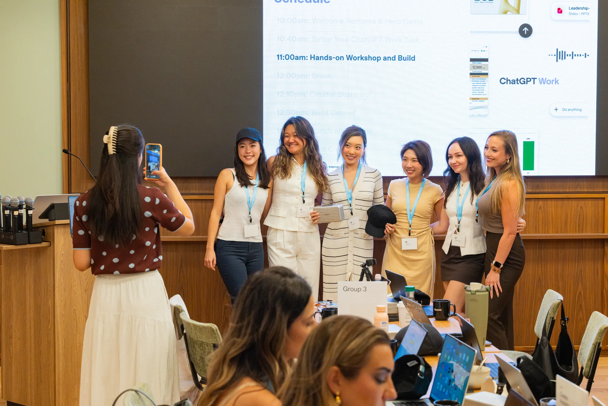 Group photo at a hands-on ChatGPT workshop: six women wearing lanyards pose at the front of the room while another takes their picture on her phone